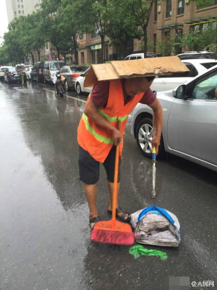 图为环卫工人头顶纸皮冒雨扫地.