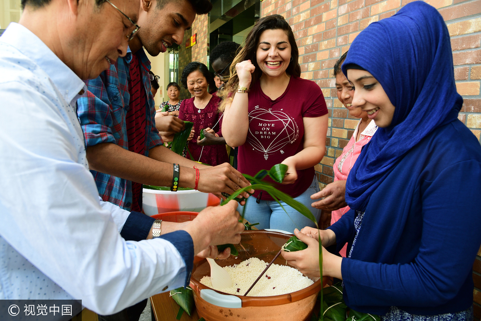 2017年5月25日，江苏镇江，社区居民在指导外国留学生包粽子。当日，端午节临近，江苏大学十多名来自赞比亚、印度、土耳其、巴基斯坦、南非等国的留学生走进镇江市和平路街道金江社区，在居民指导下学习包粽子、缝香囊，在咸鸭蛋上描画端午民俗，体验中国传统的端午文化。