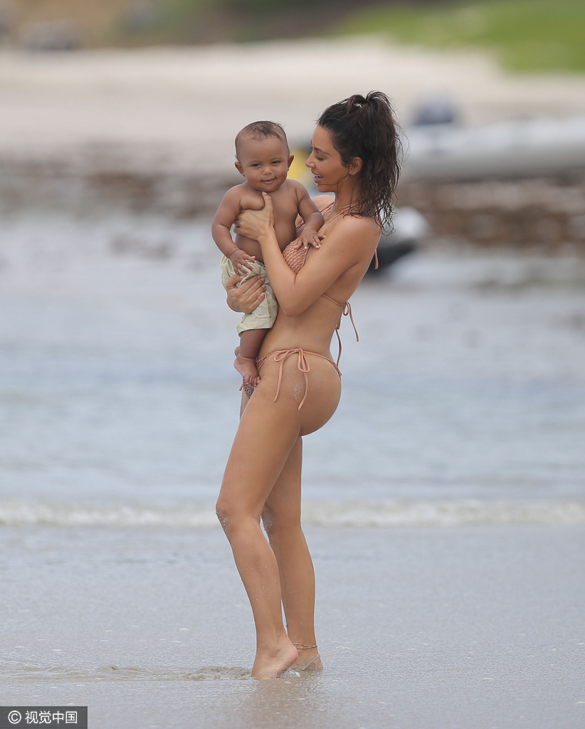 当地时间8月18日，金·卡戴珊（Kim Kardashian）带女儿小西北和儿子沙滩玩耍，卡戴珊身穿裸色系带比基尼，女儿与妈妈同款可爱十足，在沙滩上卡戴珊全程呵护幼子母爱爆棚，然而抢镜的还是翘臀。图为卡戴珊抱幼子爱意浓浓。