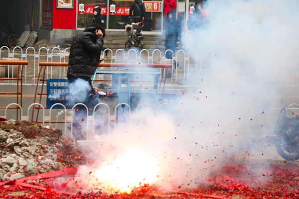 路过的行人怕被鞭炮崩到 拿衣服遮住自己的脸