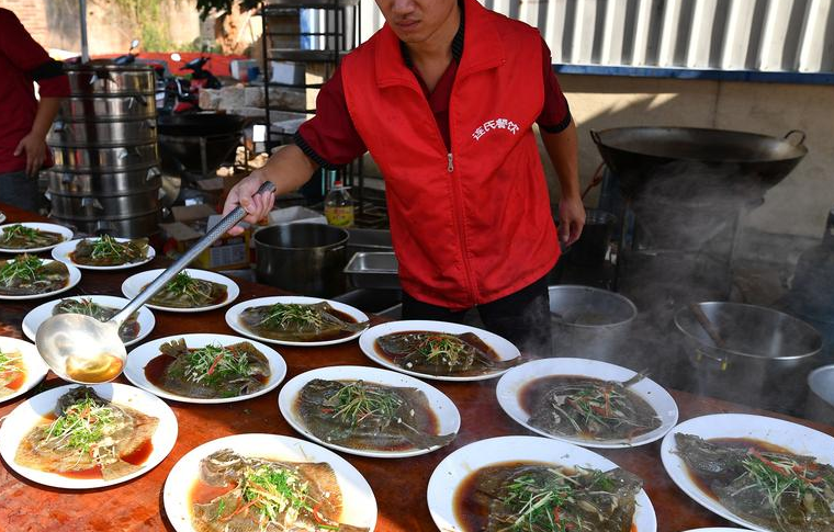 乡厨连辉腾称，虽然这次宴席的价格比较节俭，没有什么名贵的食材，但也可以达到中等水平。他做过的比较高档的宴席，一桌要三千到五千元。图为厨师往清蒸多宝鱼上浇热油。