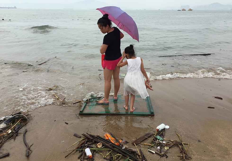 图为10月1日上午,厦门珍珠湾海滩,一对母女站在被台风吹到海里的门板上,望洋兴叹。