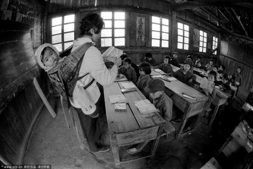 1987年4月，广西壮族自治区融水县安太乡怀村小学，戴红英老师把不满五个月的小女儿背着上课，把两岁的大女儿用绳子拴在家中。
