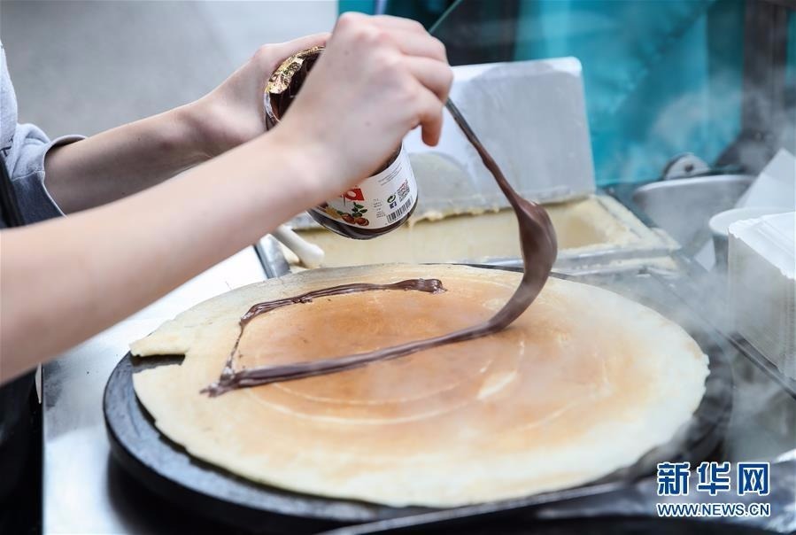 在德国首都柏林,一名可丽饼摊位的工作人员将巧克力酱涂抹在即将完成的可丽饼上。