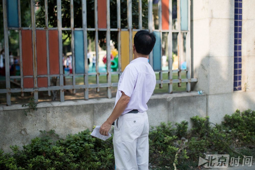 图为9月5日，浙江省杭州市一幼儿园门口，一位家长伸着脖子仔细看着园内的孩子。