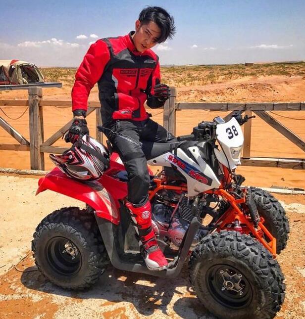 ",照片中,大东身穿红色赛车服手拿头盔,骑坐在红色山地摩托上,对着