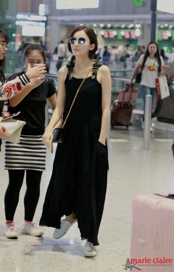 古力娜扎现身机场。她戴黑色圆框墨镜，身穿黑色背带裙，肩背Saint Laurent黑色流苏链条包，脚踩Saint Laurent白色星星印花系带休闲鞋。