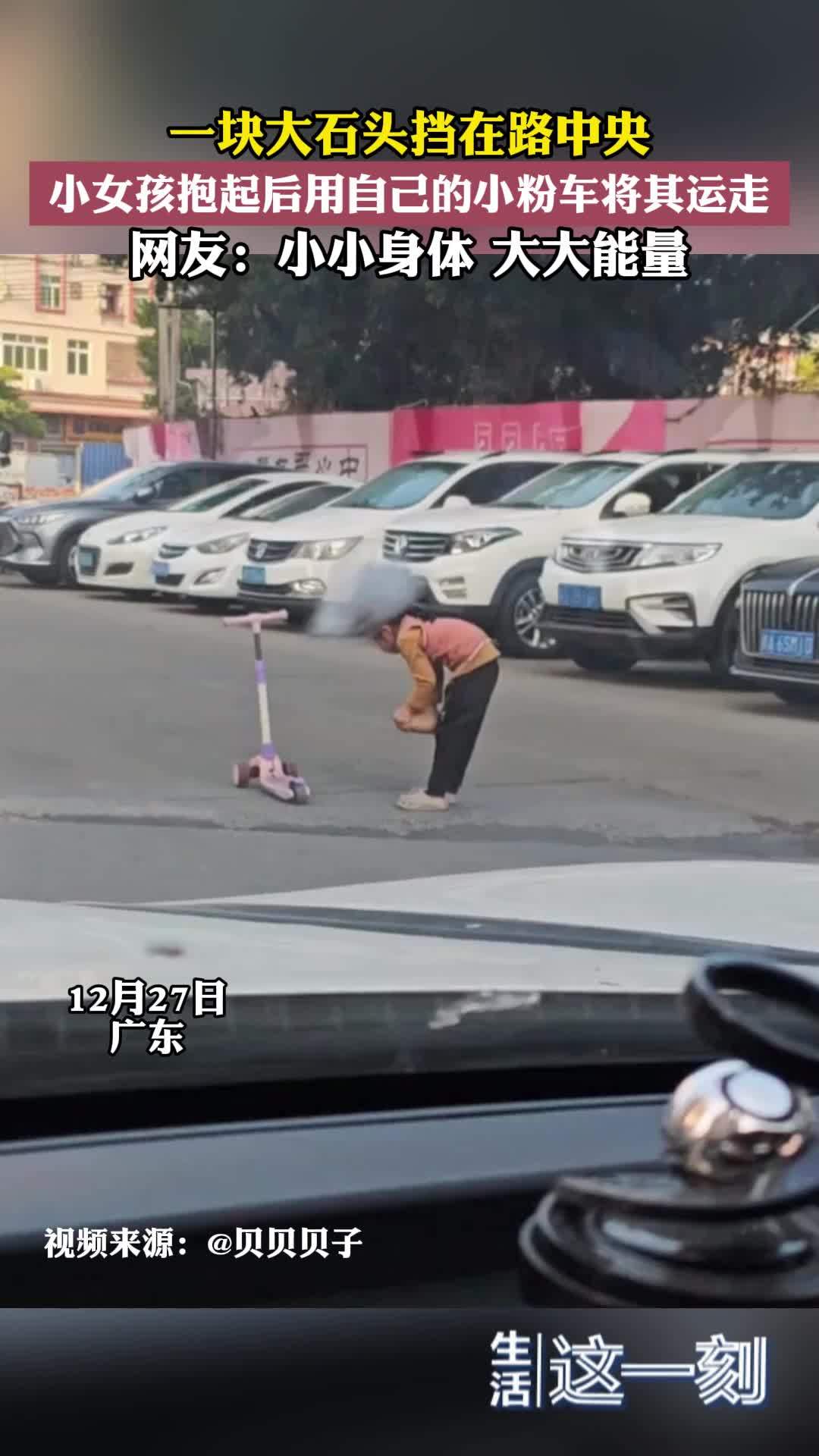 一块大石头挡在路中央  小女孩抱起后用自己的小粉车将其运